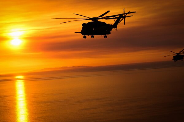 A large cargo helicopter flies into the sunset