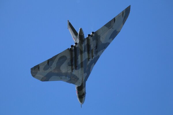 A plane in camouflage paint is flying through the sky