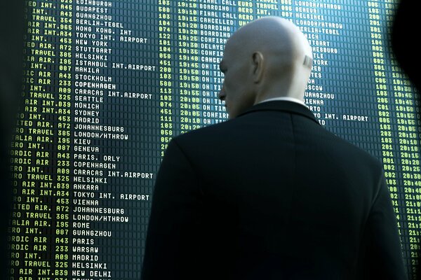 A bald man in a suit stands at the scoreboard