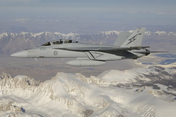 A fighter jet flies over snow-covered mountains