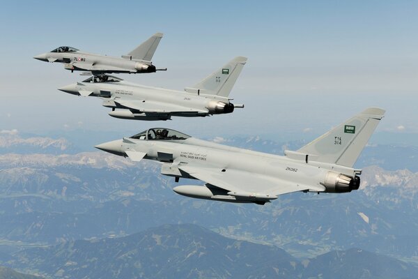 A group of fighter jets is flying over the mountains in the sky