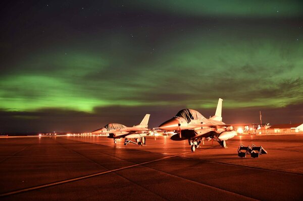 Vista nocturna del aeródromo con avión y Aurora boreal