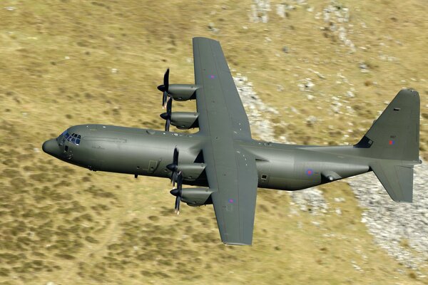 Un avión militar con cuatro hélices vuela en medio de un paisaje desértico