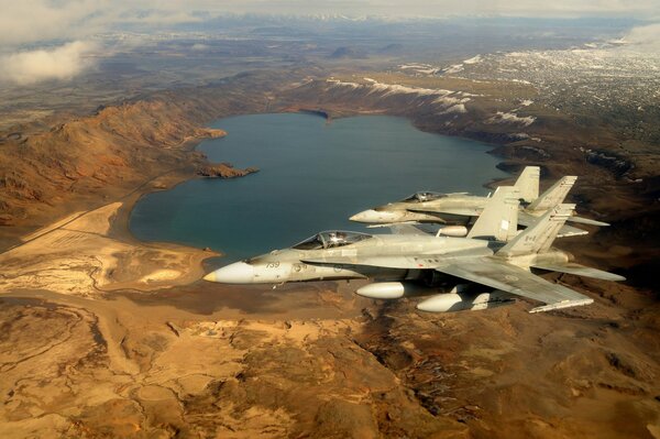 Two fighter jets are flying over a beautiful landscape