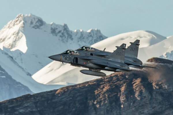 The plane flies against the background of snow-covered rocks