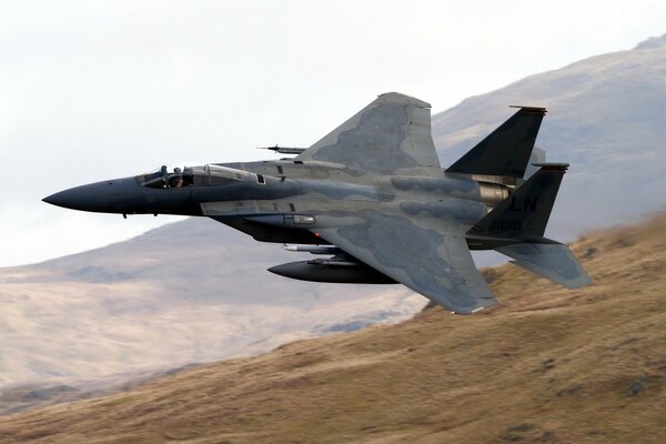 Military fighter in the sky over mountains and fields