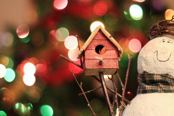 Świąteczne zabawki bałwan i domek dla ptaków na tle girlandy