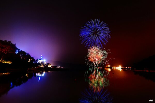 Fireworks over the city are reflected in the lake