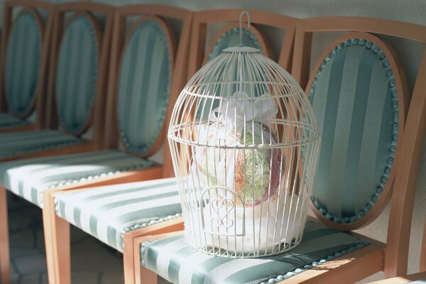 Una jaula blanca con un ramo en el interior se coloca en una silla tapizada en seda verde