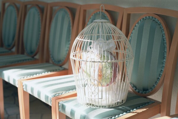 La cage blanche avec le bouquet à l intérieur se tient sur la chaise tapissée par soie verte