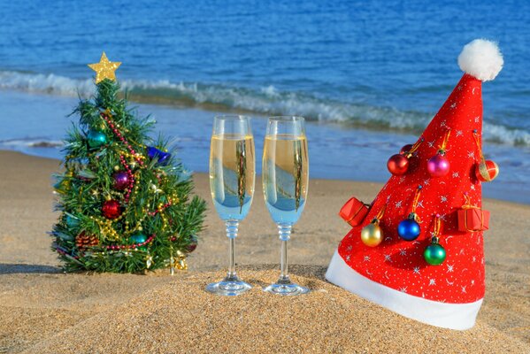 Árbol de Navidad, sombrero de Santa Claus y dos copas de champán en la playa del océano