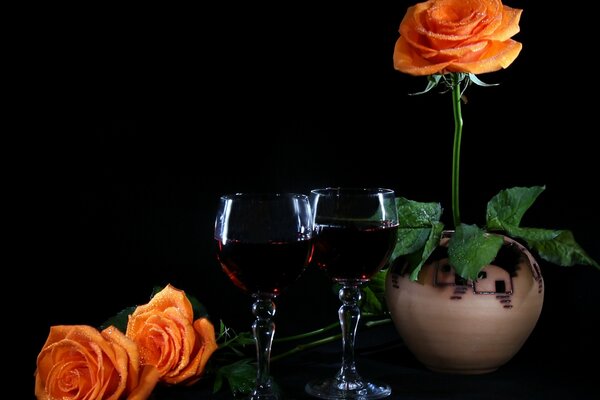 An orange rose in a pot and two glasses of wine