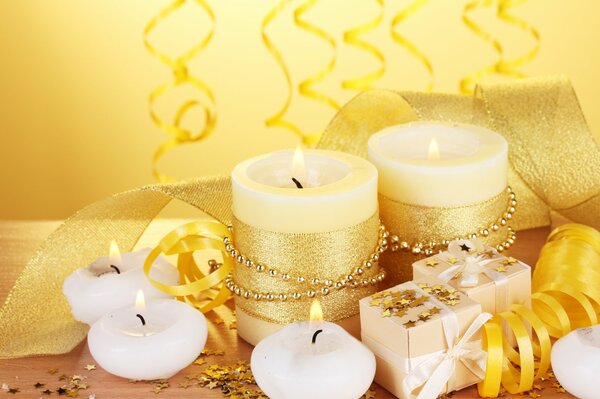 Gold and white burning candles next to gift boxes