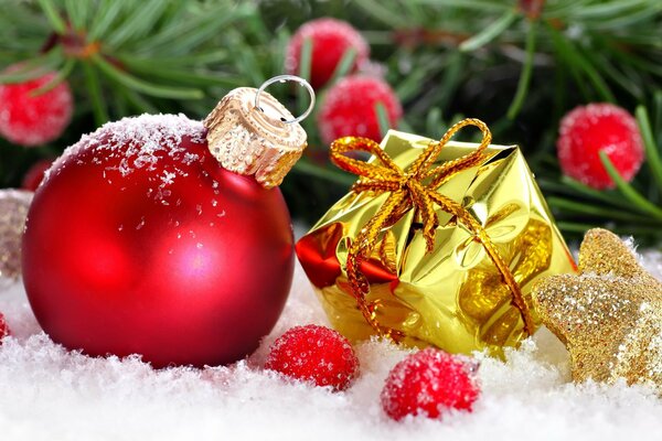 Una bola roja y un regalo en un paquete amarillo acostado en la nieve