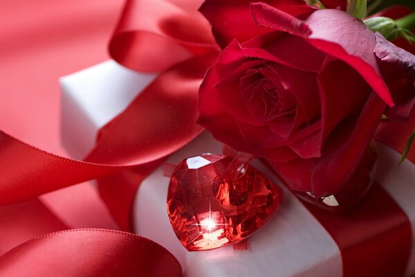 A precious stone lies on a gift box next to a rose