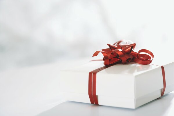 Белая подарочная коробка перетянутая красной лентой и бантиком