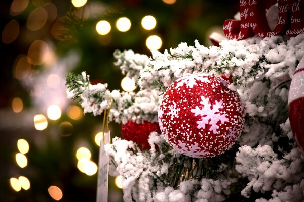 A red shimmering ball with snowflakes on a snow-covered fir branch