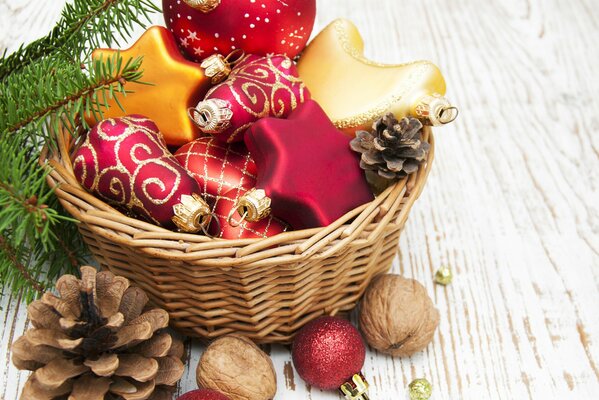 Red and gold Christmas tree toys in a basket with cones and nuts on a wooden board