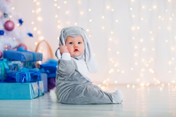 Bebé en traje de conejito en el árbol de Navidad