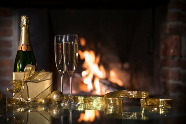 Sobre la mesa hay una botella de champán, copas y un regalo. En el fondo se quema la chimenea