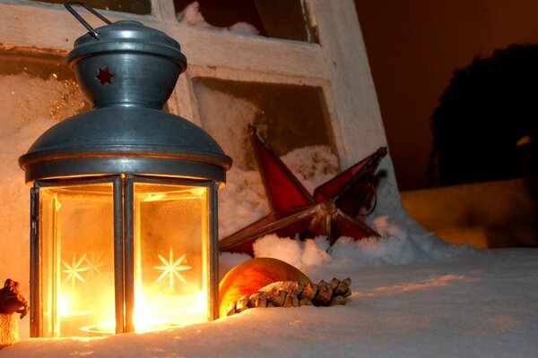 Candela lanterna a mano di Natale nella neve e bastoncini di cannella