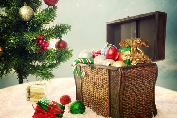 A Christmas landscape with a box of Christmas decorations on a beige fluffy blanket and a green spruce decorated with toys