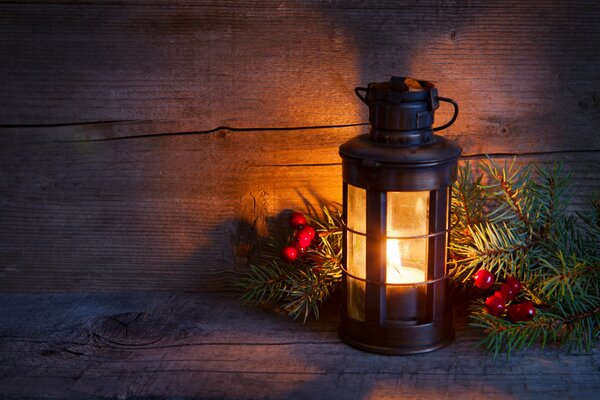 A candle burns in a lantern next to a fir branch