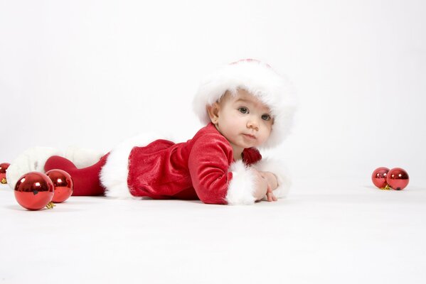 A kid in a Santa Claus costume on a white background with red Christmas toys