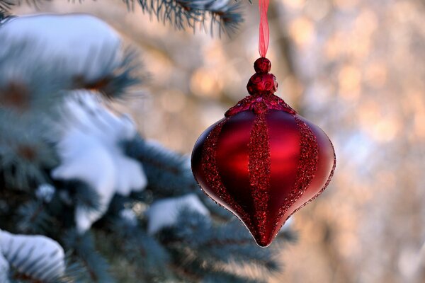 A red toy is hanging on a branch of a snow tree