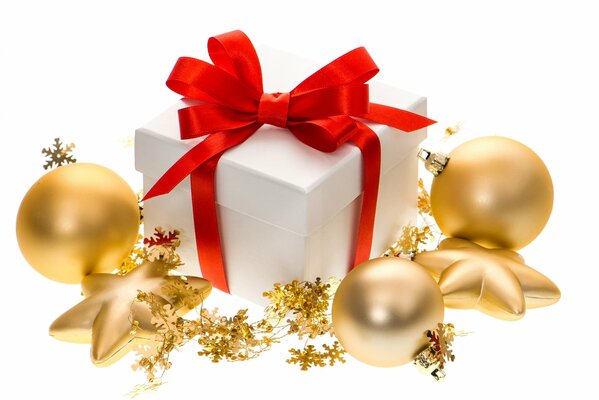 Regalo di Capodanno in scatola bianca con nastro rosso tra palle di Natale e stelle in design dorato su sfondo bianco