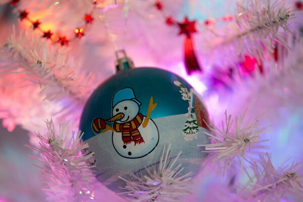 Christmas toy - a ball with a snowman, hanging on a white Christmas tree