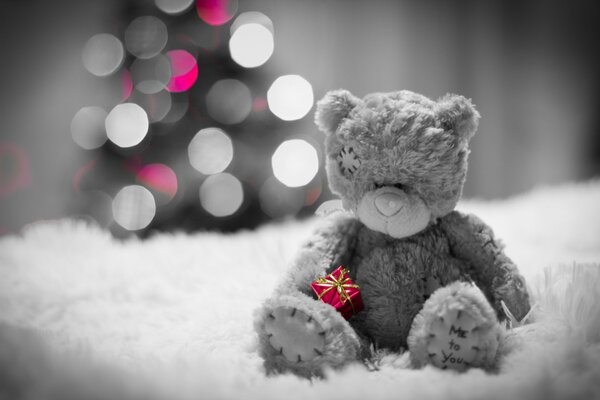 The bear is sitting near the Christmas tree