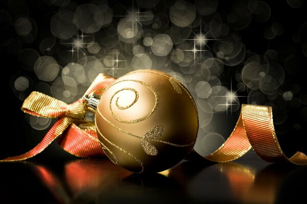 Новогоднее ёлочное украшение в виде золотого шара с лентой на чёрном фоне