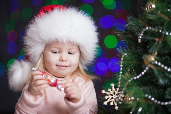 The girl unwraps a candy near the Christmas tree