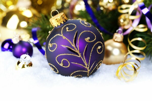 Bola de año nuevo púrpura en la nieve bajo una rama de abeto