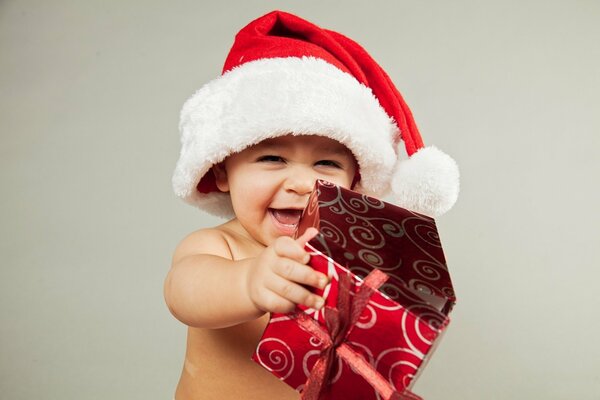 Bambino sorridente in un cappello di Babbo Natale e con un regalo