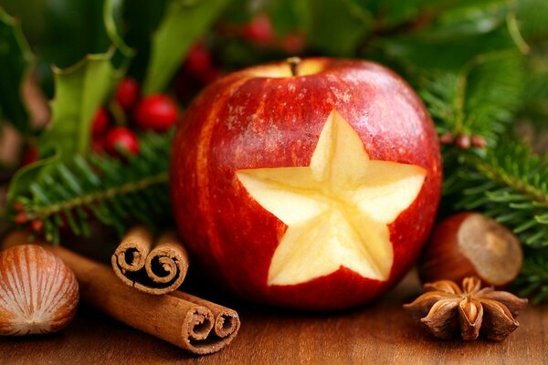 An apple with a star-shaped cutout and cinnamon near the Christmas tree