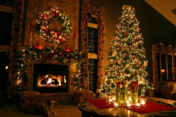 A Christmas decorated fir tree by a burning fireplace with a Christmas wreath and fir decorations hanging over it