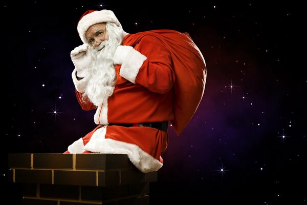 Powitalny machający ręką i uśmiechnięty Święty Mikołaj z torbą prezentów siedzi na rurze