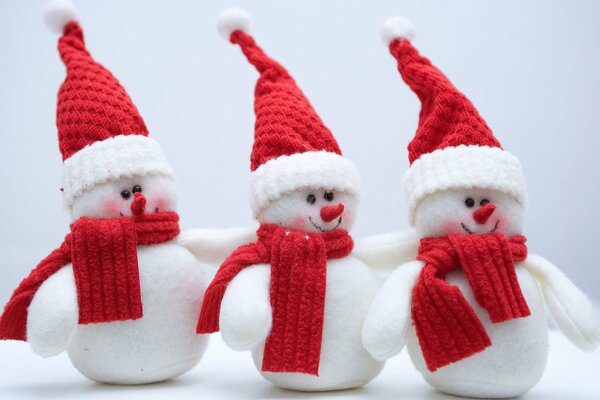 Tres muñecos de nieve en bufandas rojas y gorras