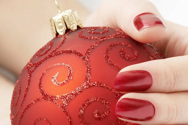 A hand with a red manicure holds a red Christmas tree toy