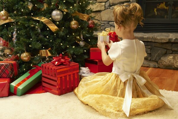 Niña con un vestido con regalos cerca del árbol de Navidad