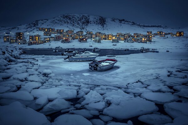 Evening village on the coast. Boats on cracking ice floes