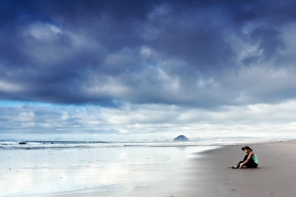 A girl is sitting on the ocean shore on the sand