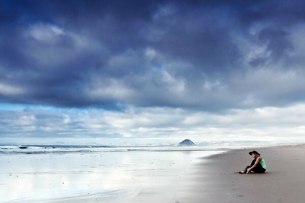 Chica sentada en el océano en la arena