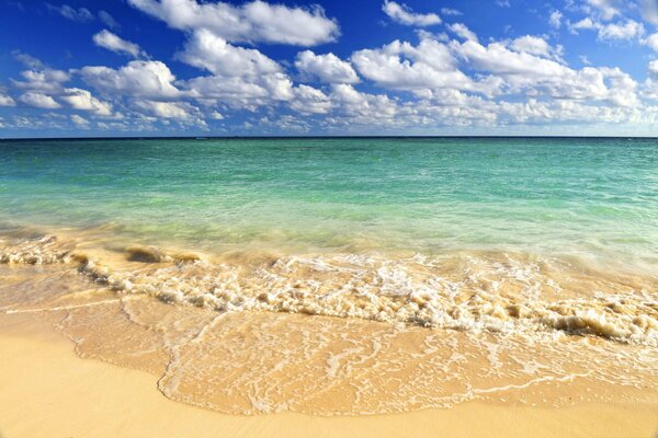 Ein Sandstrand mit blauen Wellen und schönen Wolken