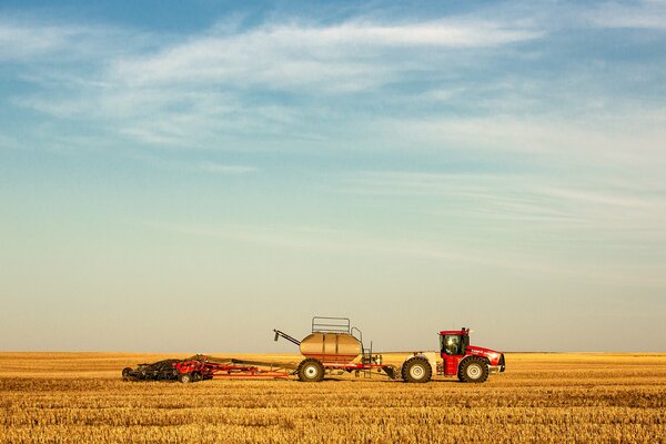 Traktor auf dem Hintergrund des gelben Feldes und des blauen Himmels