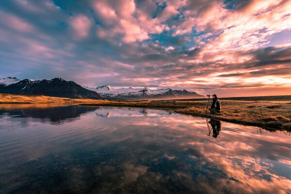 Фотограф на берегу озера снимает закат в горах