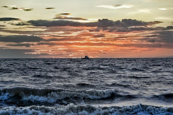 Schiff im Hintergrund des Sonnenuntergangs im tobenden Meer