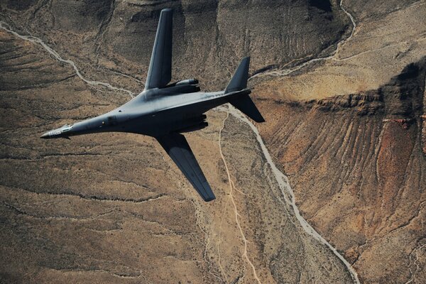 A supersonic grey b-1b strategic bomber is flying over the landscape